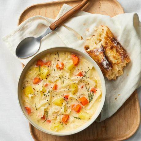 Un plato de sopa cremosa de patatas y repollo junto a una cuchara y un trozo de pan tostado